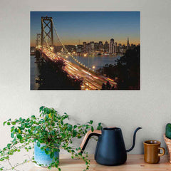 Poster of a Golden Gate Bridge and cityscape at dusk, placed on a wall above a table with a plant and kitchen items.